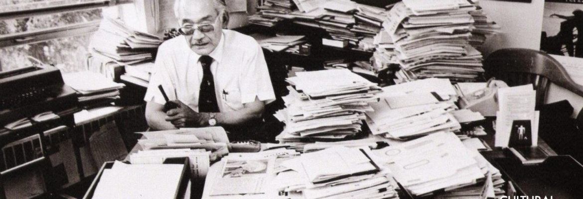 Min Yasui at his desk piled with papers